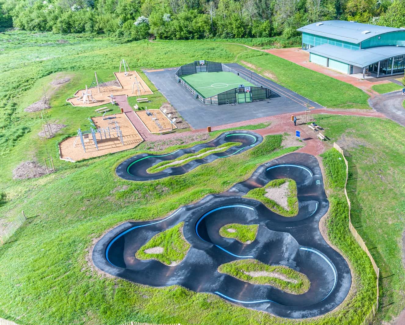 Drohnenaufnahme einer Freizeitanlage in Cublize mit Pumptrack, Sportplatz, Spielplatz und einer Sporthalle.