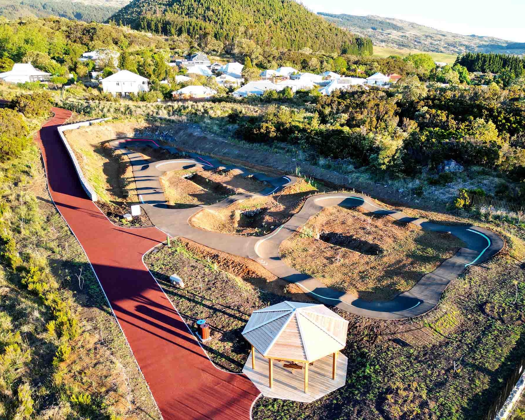 Aerial view of the complete pump track facility in Le Tampon featuring a wooden gazebo and residential area.
