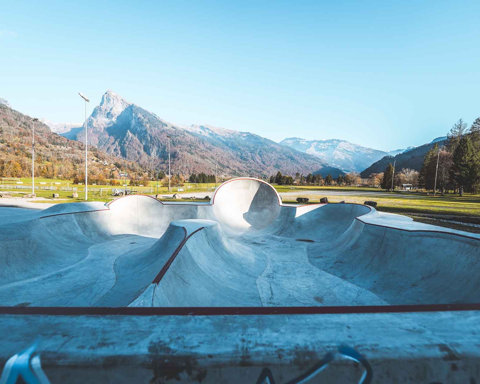 Overview of the bowls and ramps of the Samoëns skate park with a view of the surrounding mountains.