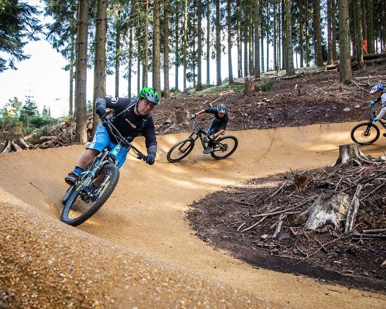 [Translate to Chinesisch:] Zwei Biker fahren eine Kurve auf einem neu gebauten Bikepark im Wald