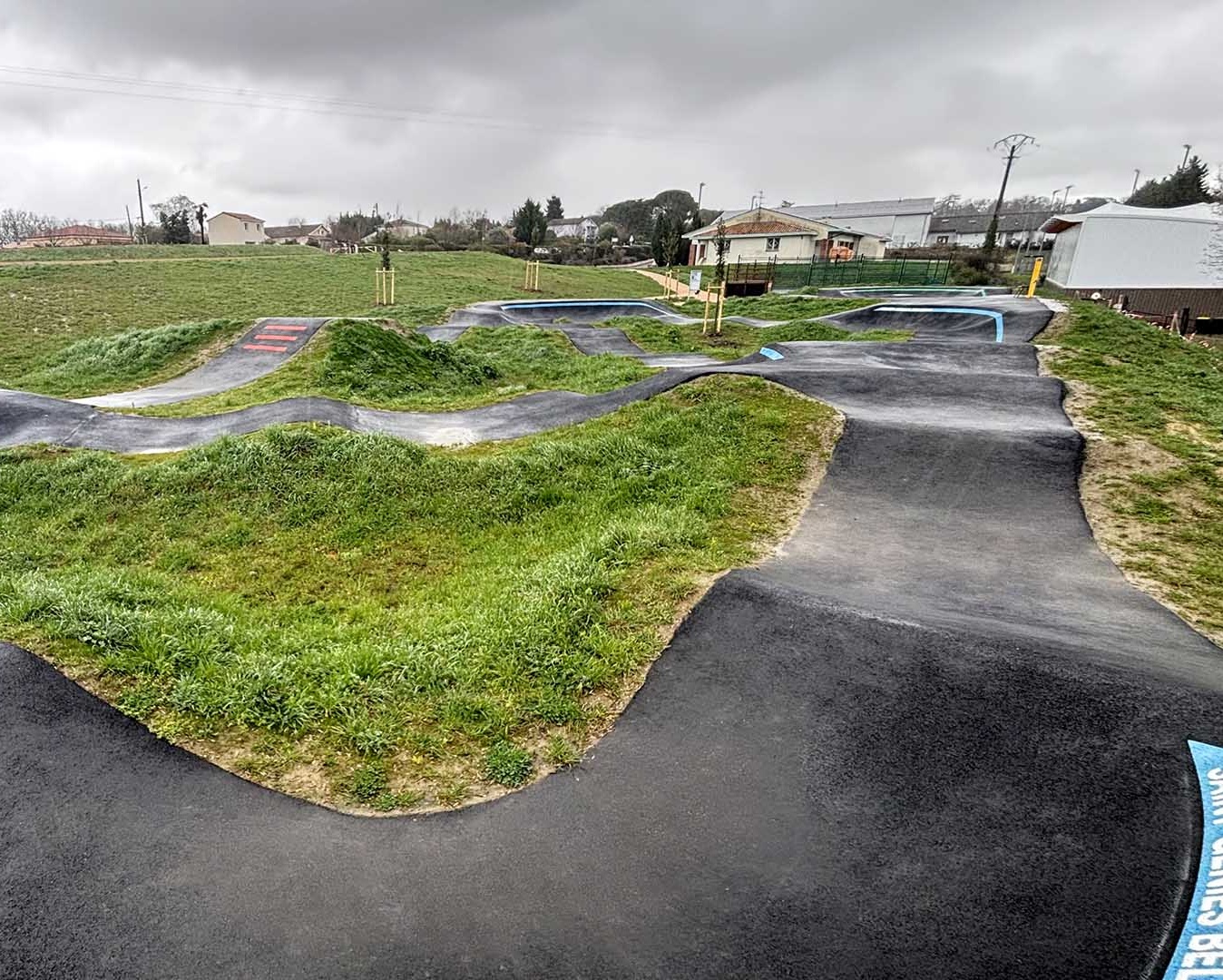 Wide-angle overview of the spacious pumptrack in Saint-Geniès-Bellevue under a cloudy sky.